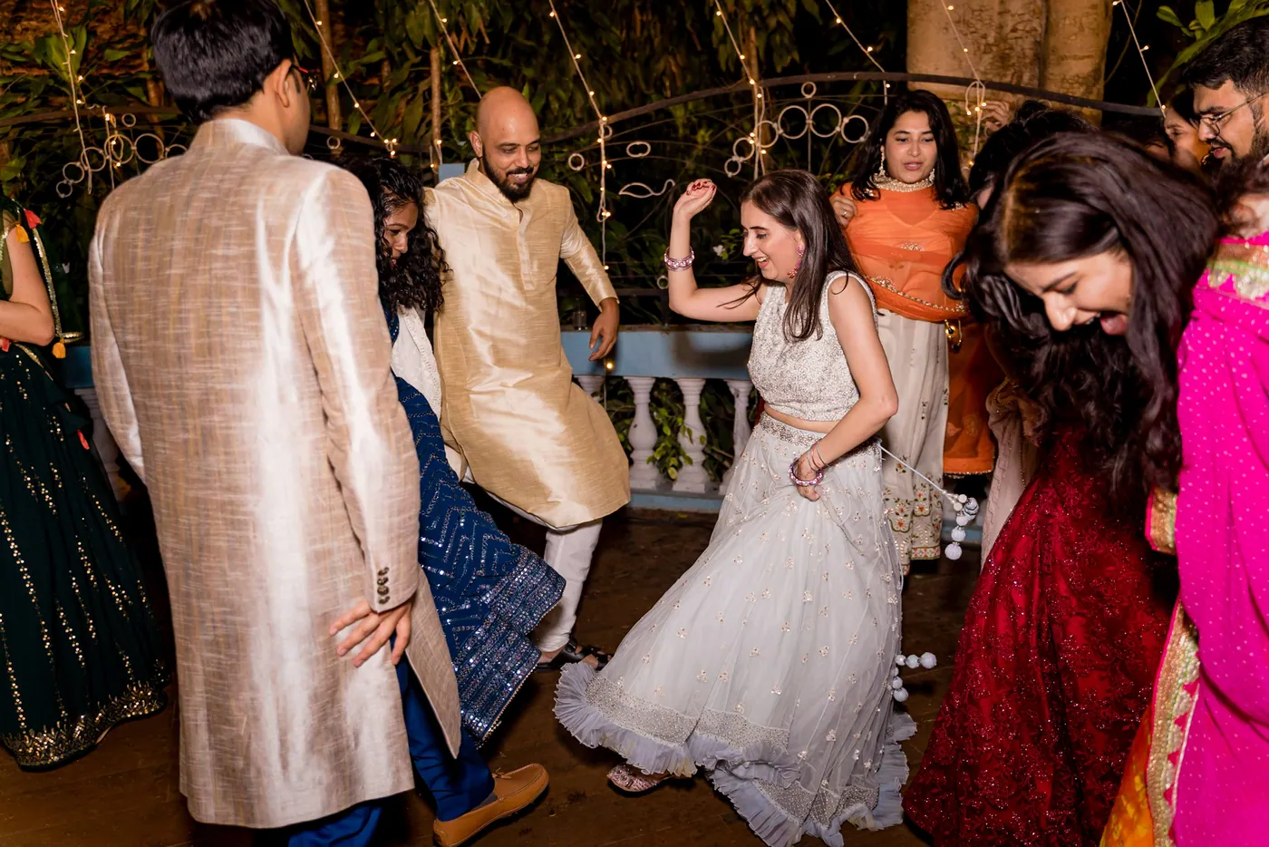 A man in a gold kurta turns away as a woman in a white lehenga dances with her hair swinging