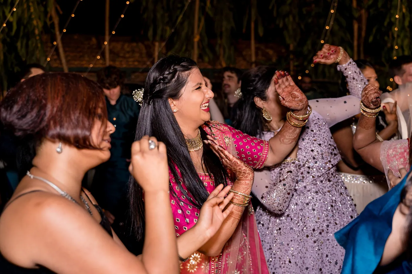 A woman in a pink blouse and others in lilac and cream dance closely with open mouths