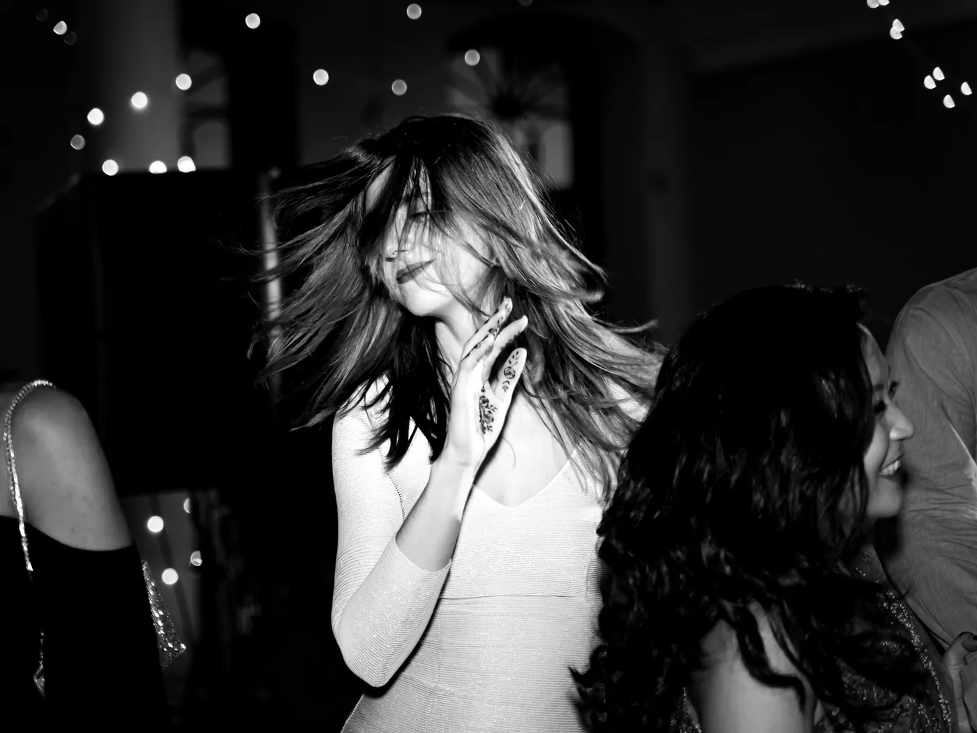 In black and white, a woman in a pale dress flings her hair as she dances