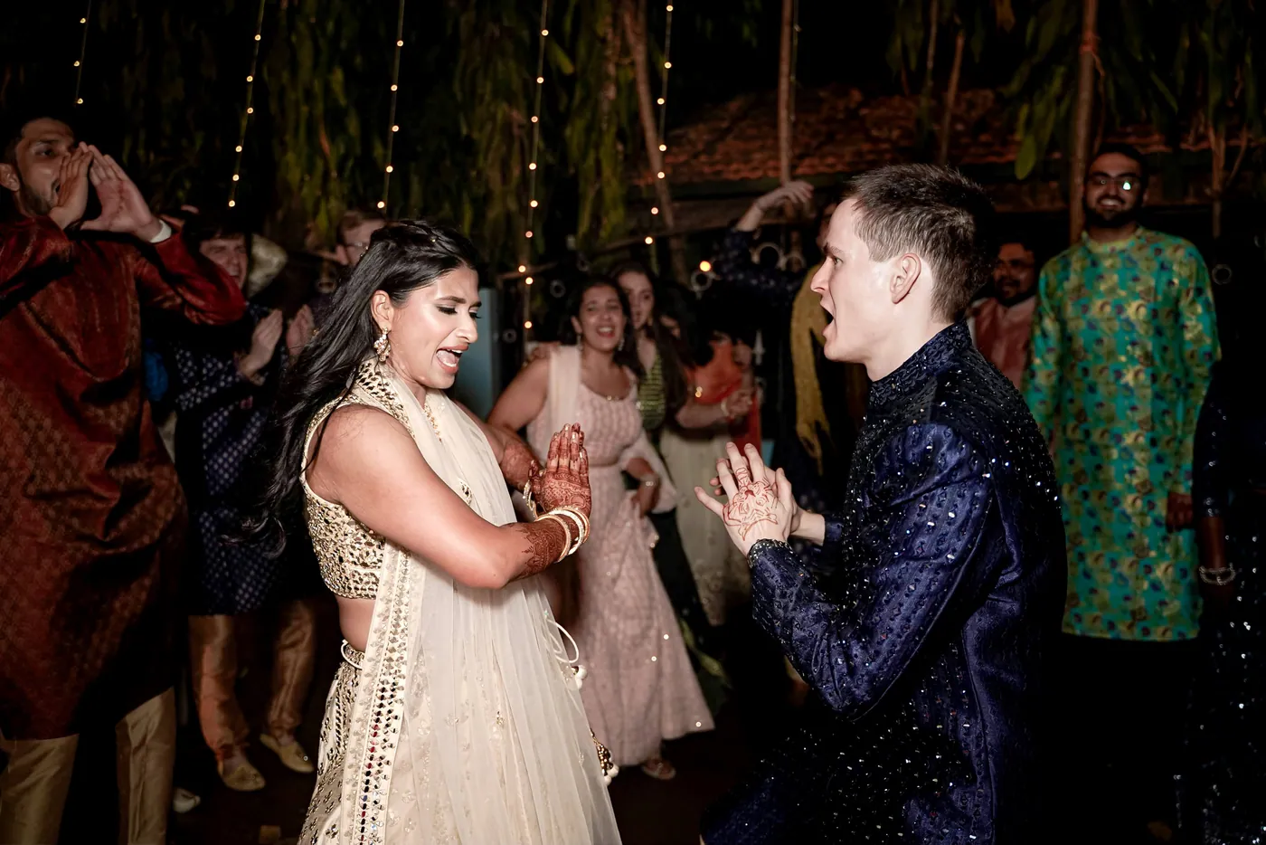 Medha dances beside Stefan, hands clasped in front of her, with guests behind them