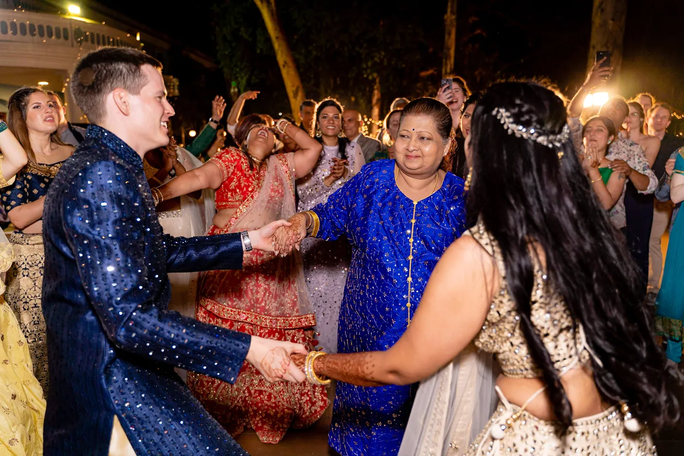Stefan and Medha hold hands with a woman in a bright blue kurta as the three dance together