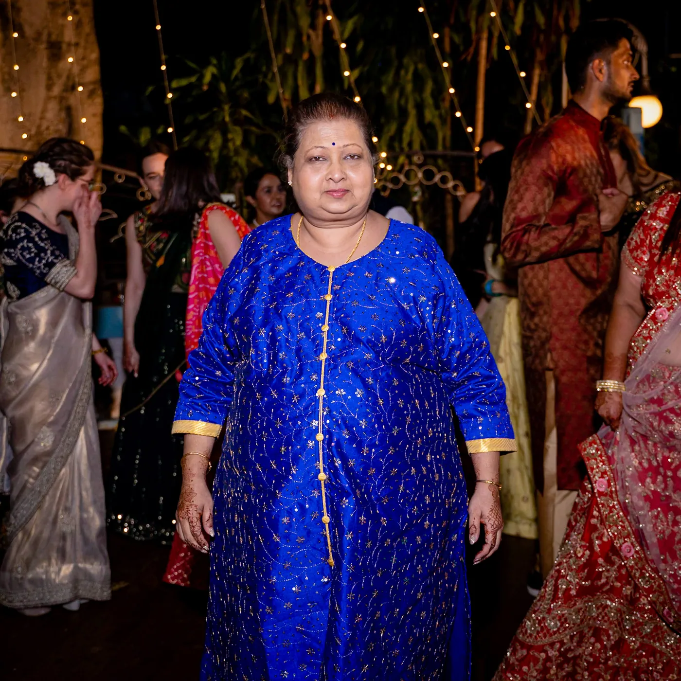 A woman in a bright blue kurta stands still in the middle of the dance floor, surrounded by dancers