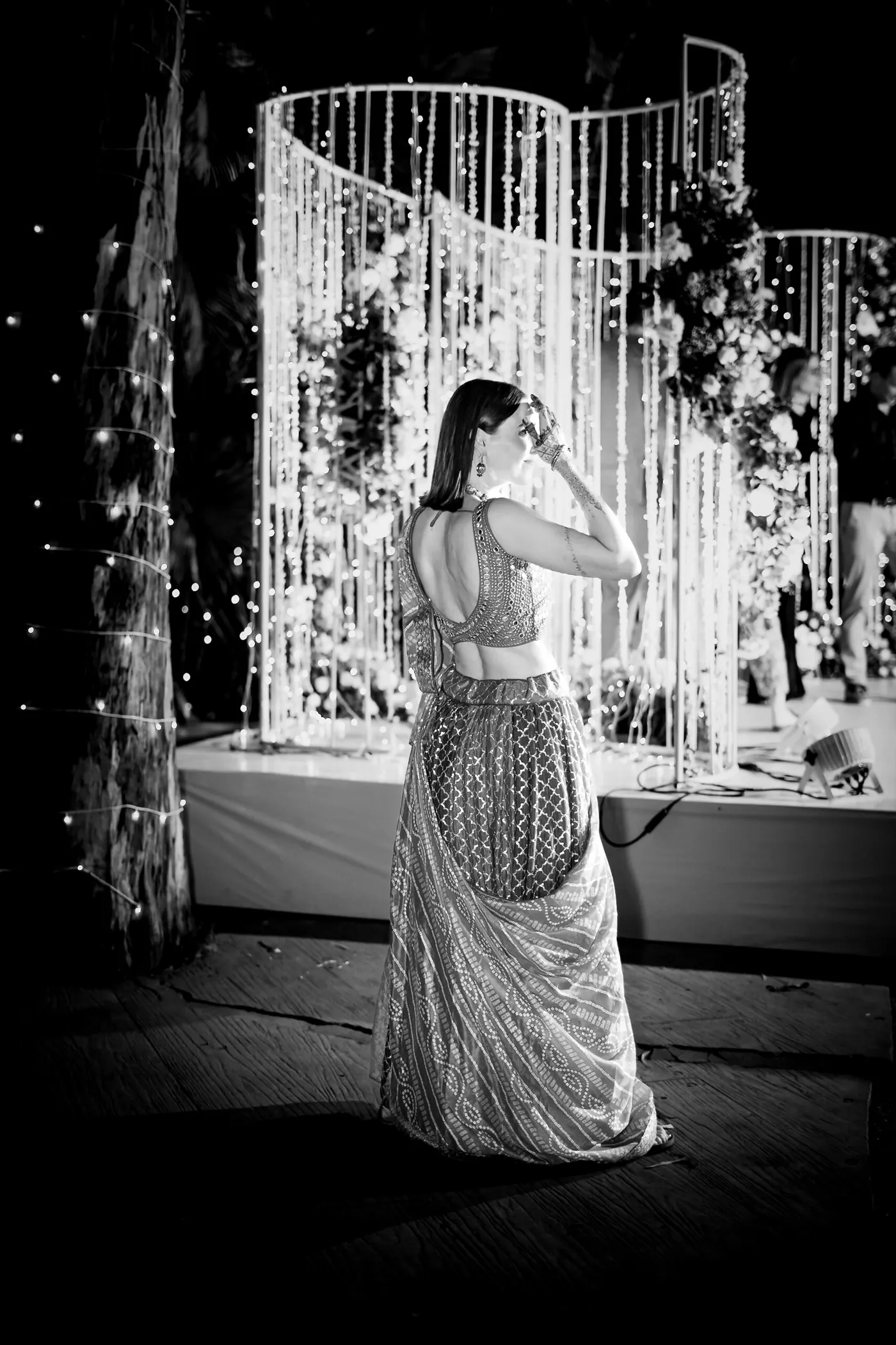In black and white, a woman stands on the stage with her back to the camera facing the lights