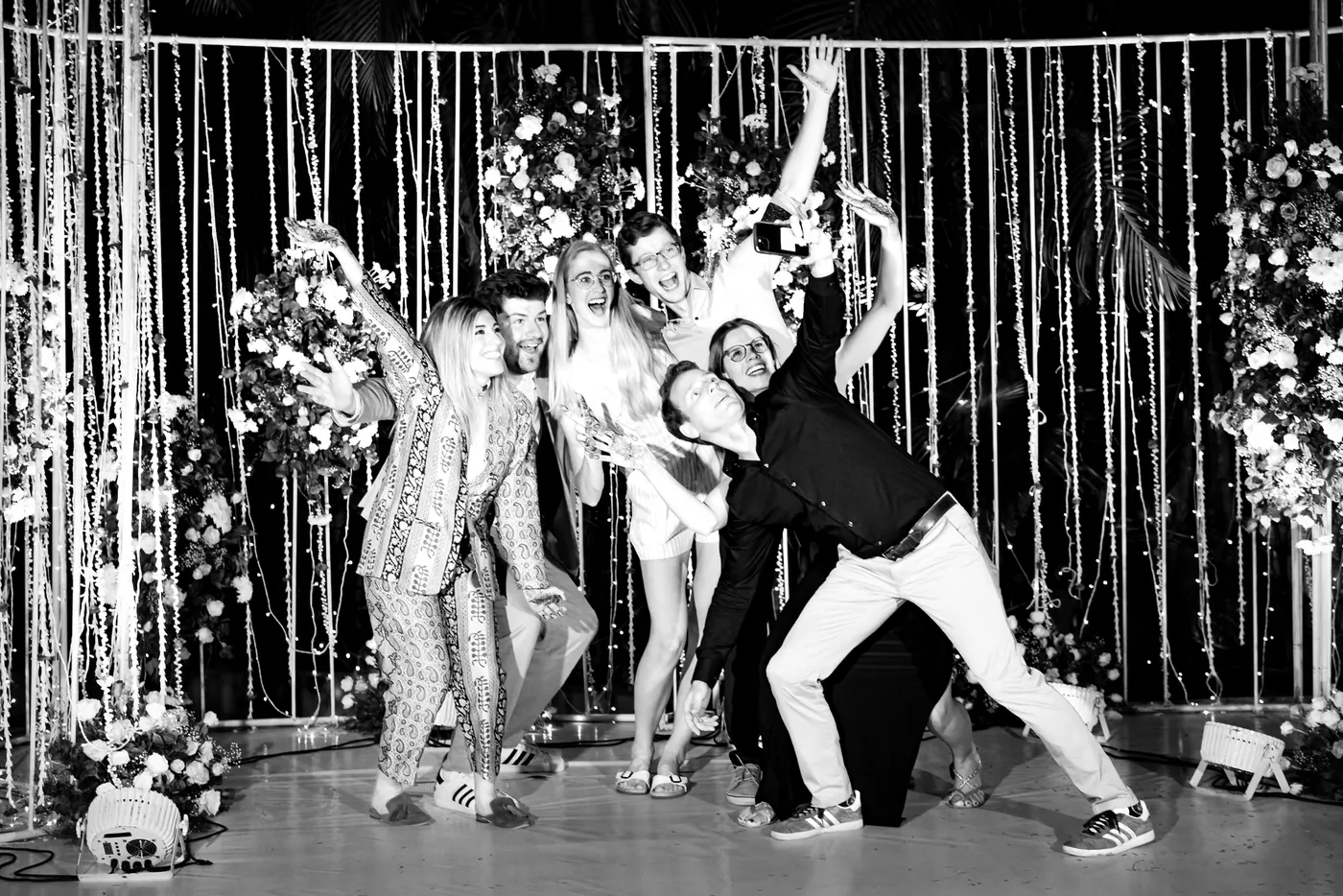 In black and white, friends dance on the stage with arms flung wide, one leaning far to the side