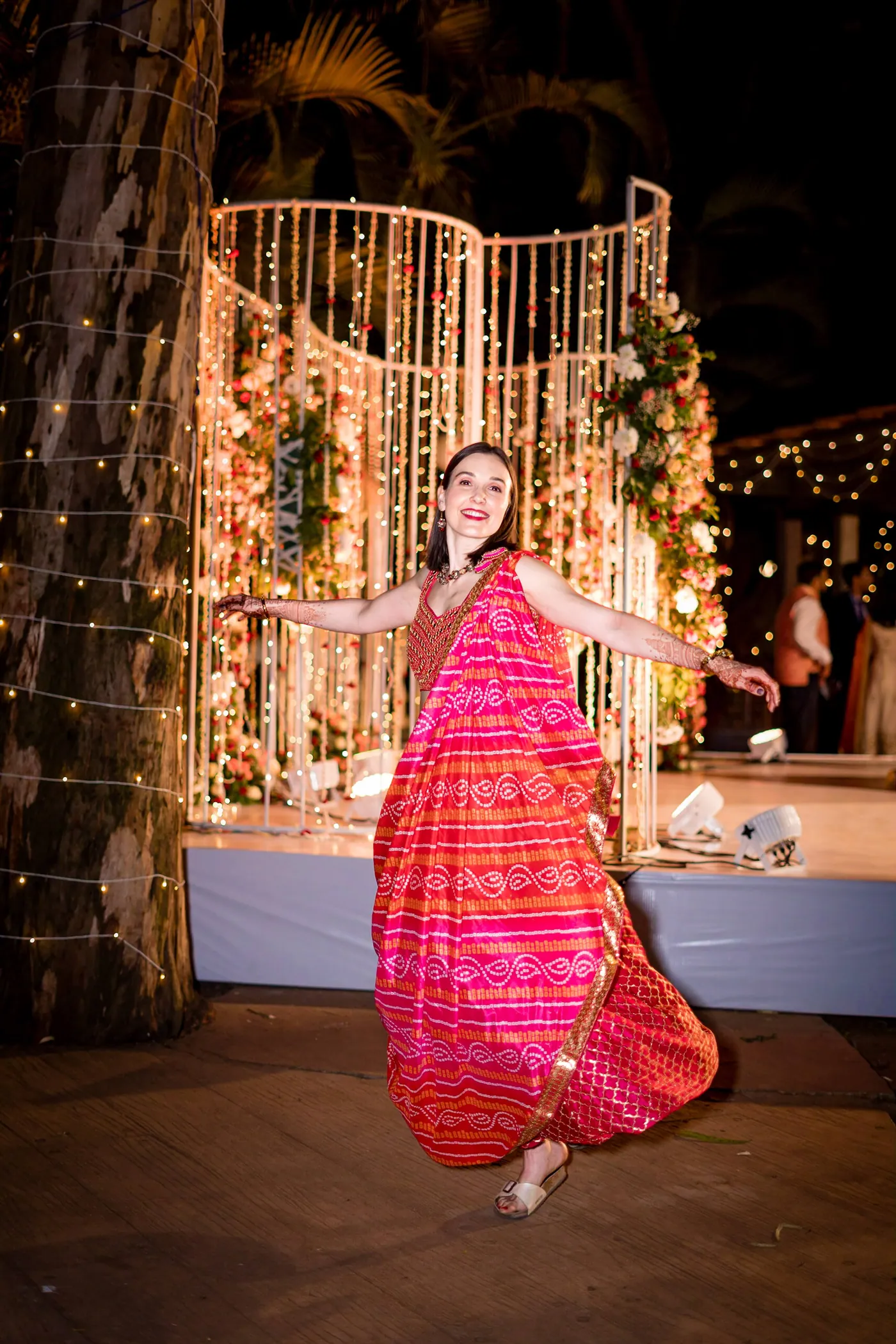 Stefan's sister dances in a bright red and orange sari on the stage, arms held wide