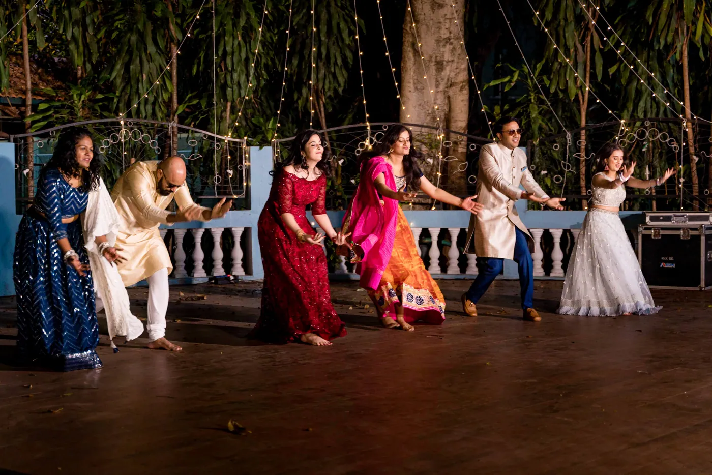A line of dancers in saris, lehengas and kurtas performs in step across the wooden floor
