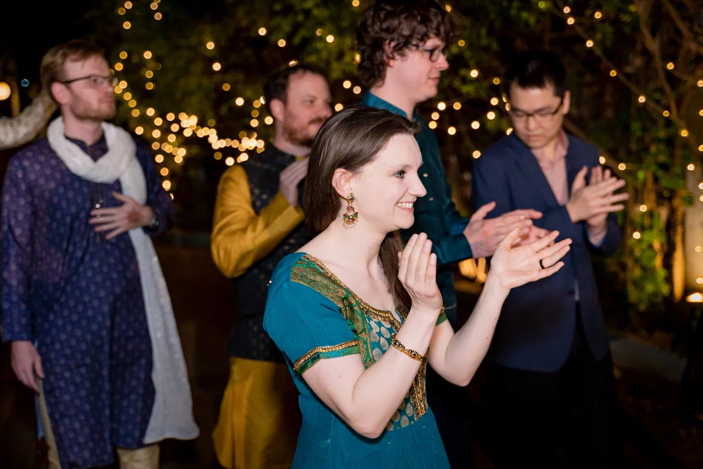 Guests clap and cheer along as a woman in a teal outfit smiles at the front
