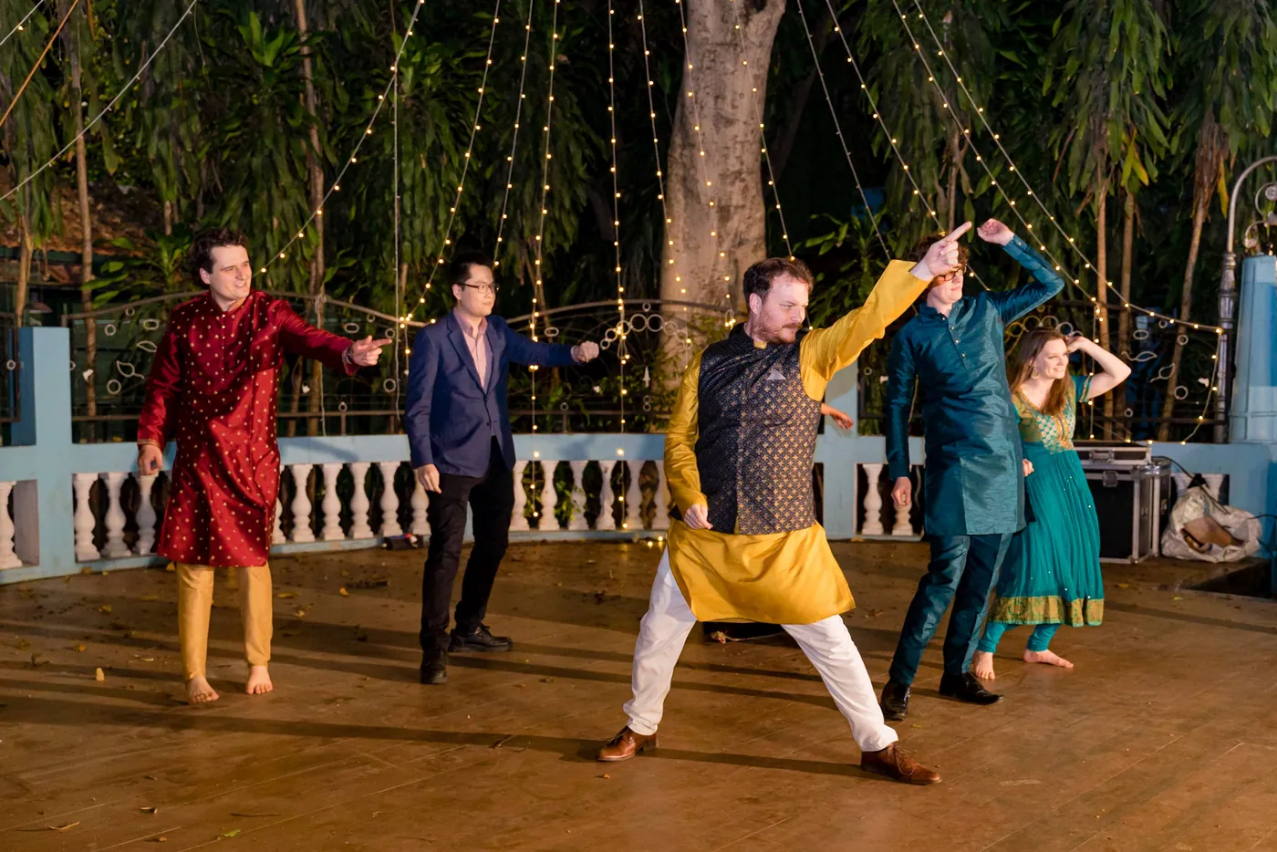 Men in red, yellow and teal kurtas strike a wide legged pose mid routine