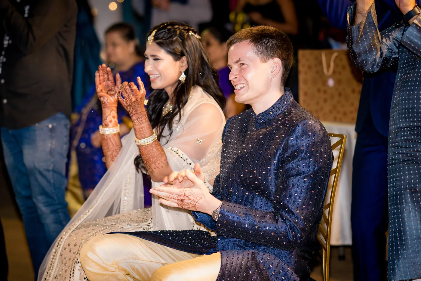 Medha laughs with her hands up, her mehendi showing, as Stefan sits next to her in the front row