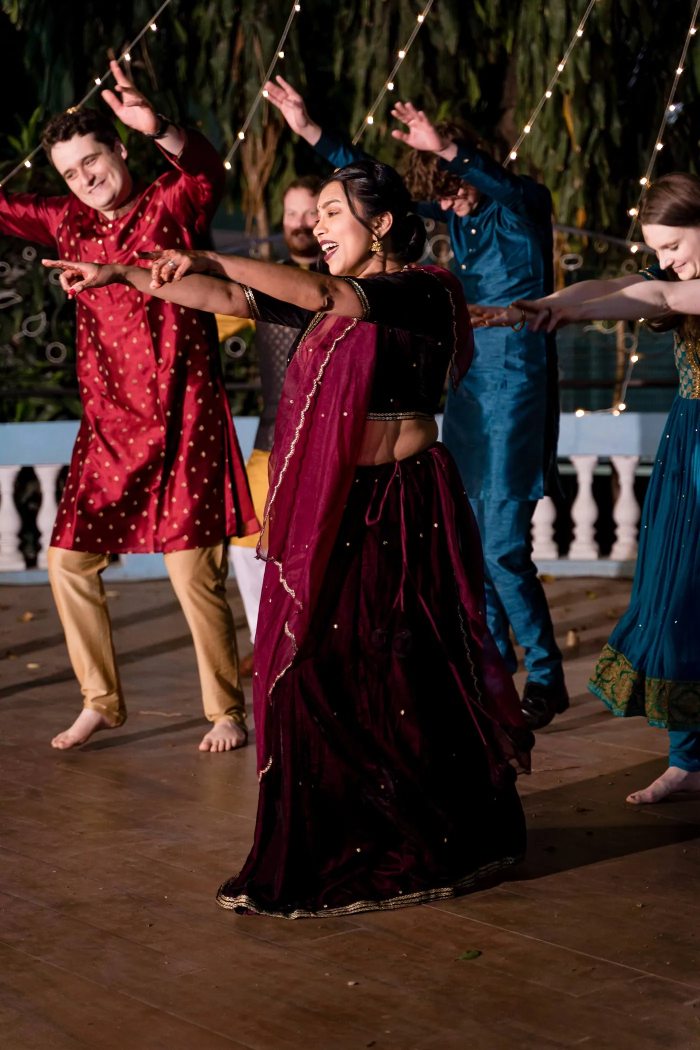 A man in a red kurta and a woman in a maroon skirt dance together with one arm out