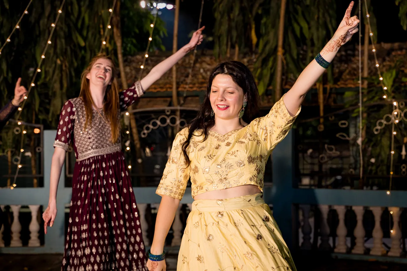 Two women in a maroon top and a yellow top raise their arms and laugh as they dance