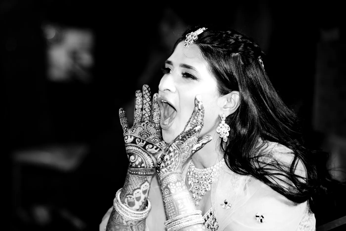 In black and white, Medha throws her henna covered hands to her face with a laugh