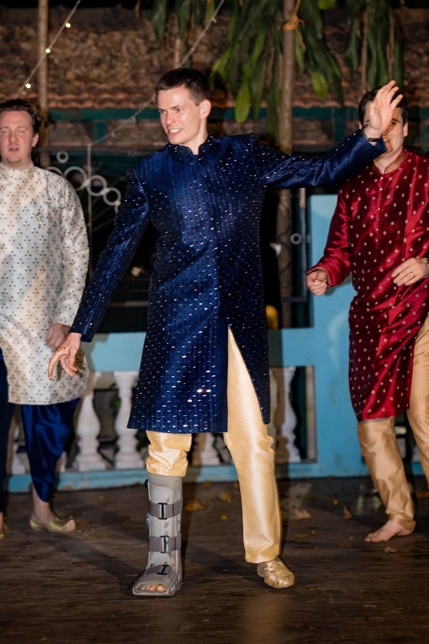 Stefan in a navy sherwani dances mid step with a medical boot on his ankle