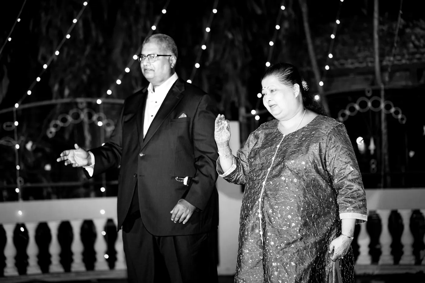 In black and white, a man in a tuxedo and a woman in a sparkling kurta dance side by side