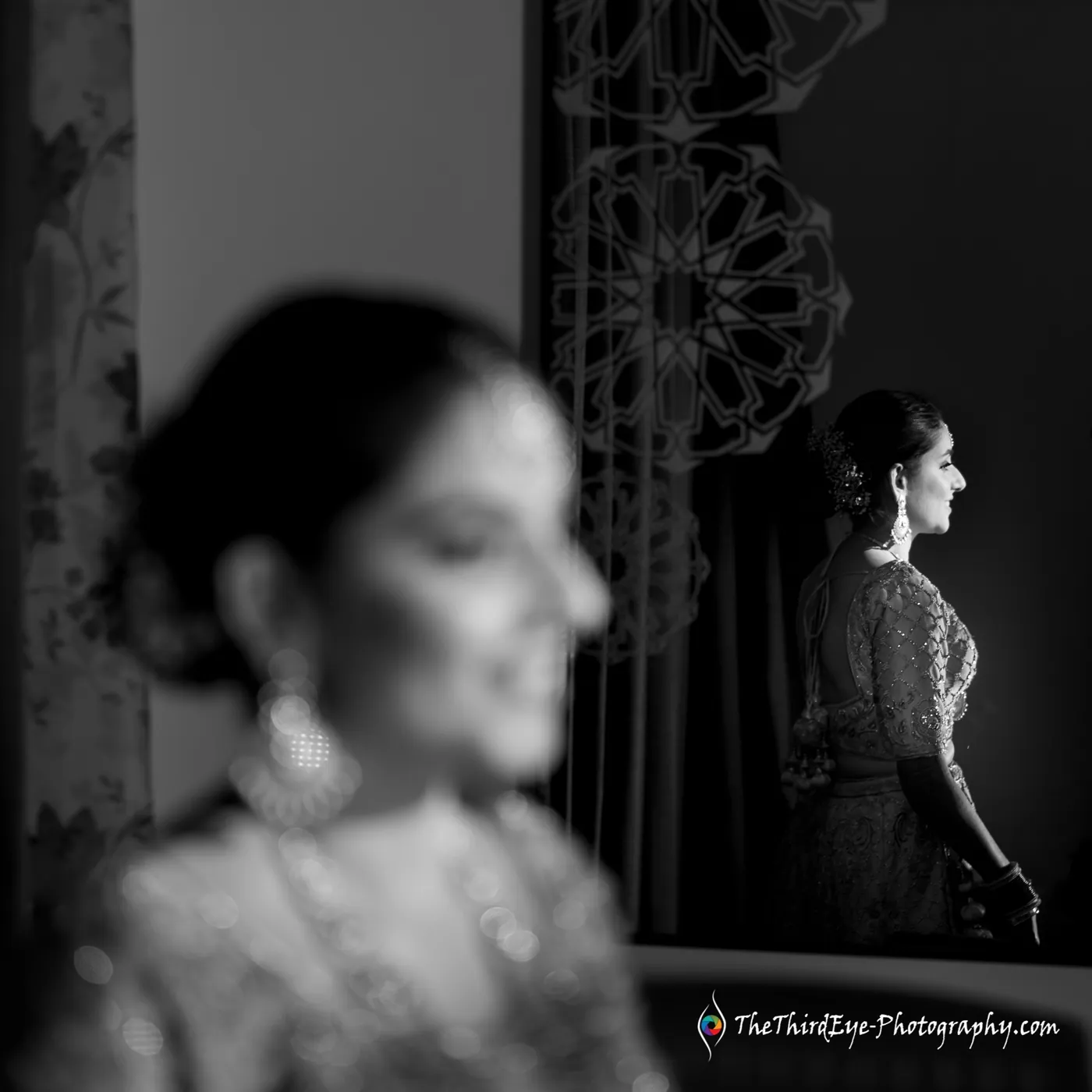 Black and white frame of the bride's face blurred in the foreground as her profile glows in a mirror behind