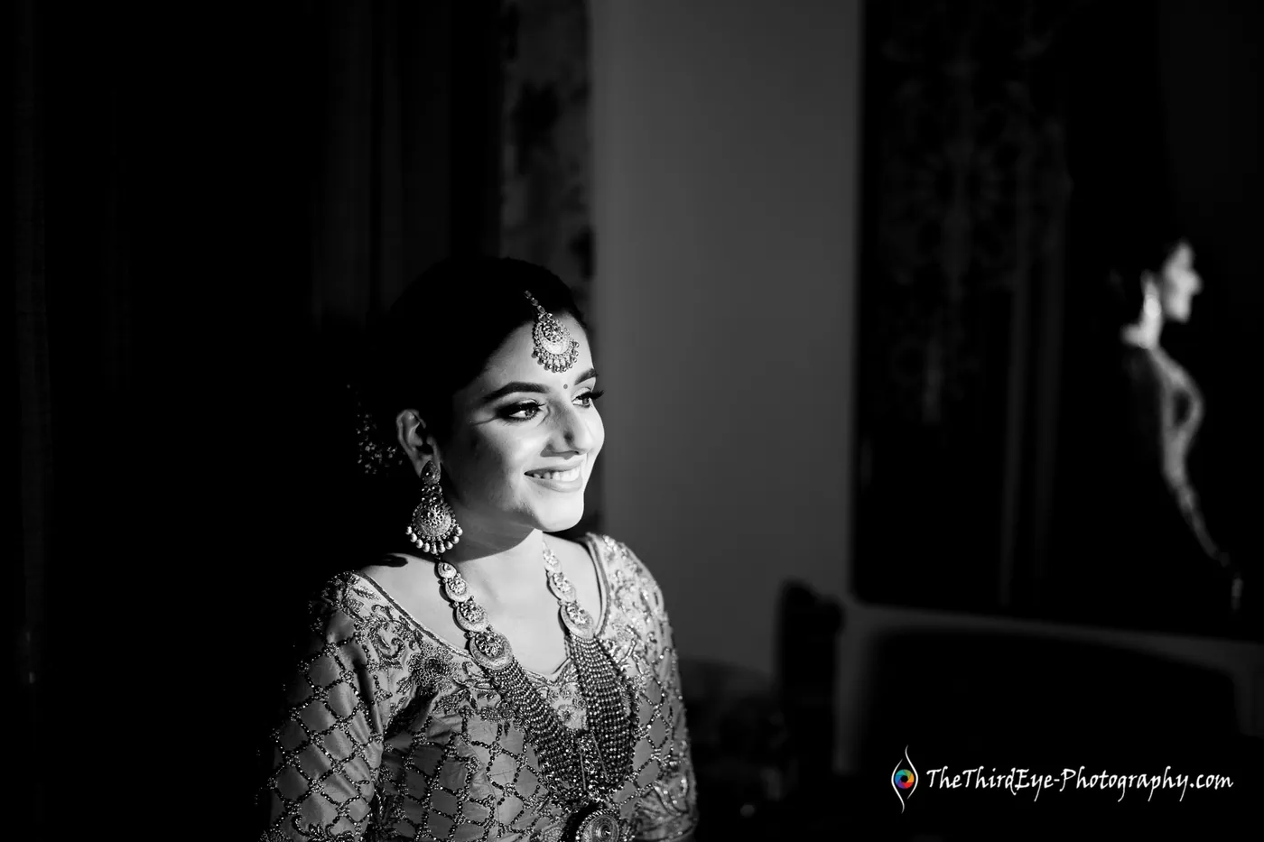 Black and white frame of the bride smiling in a dark corridor, lit only from one side