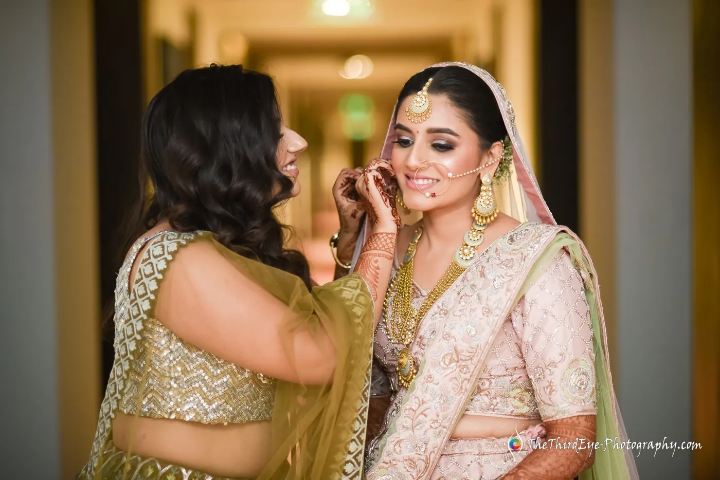 A woman reaches up to adjust the bride's earring in a dim hallway as both smile