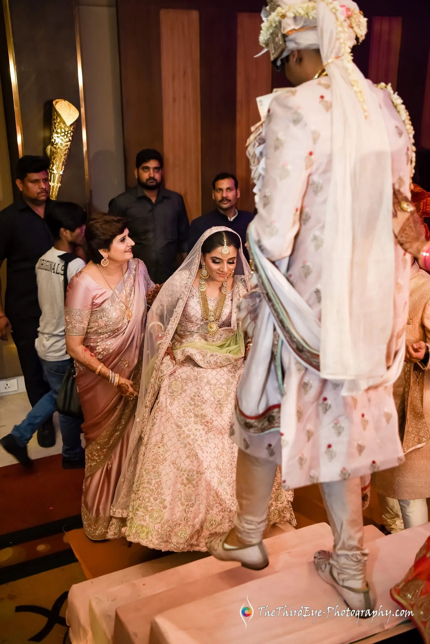The groom stands on a raised box towering over the bride as women and relatives gather around them