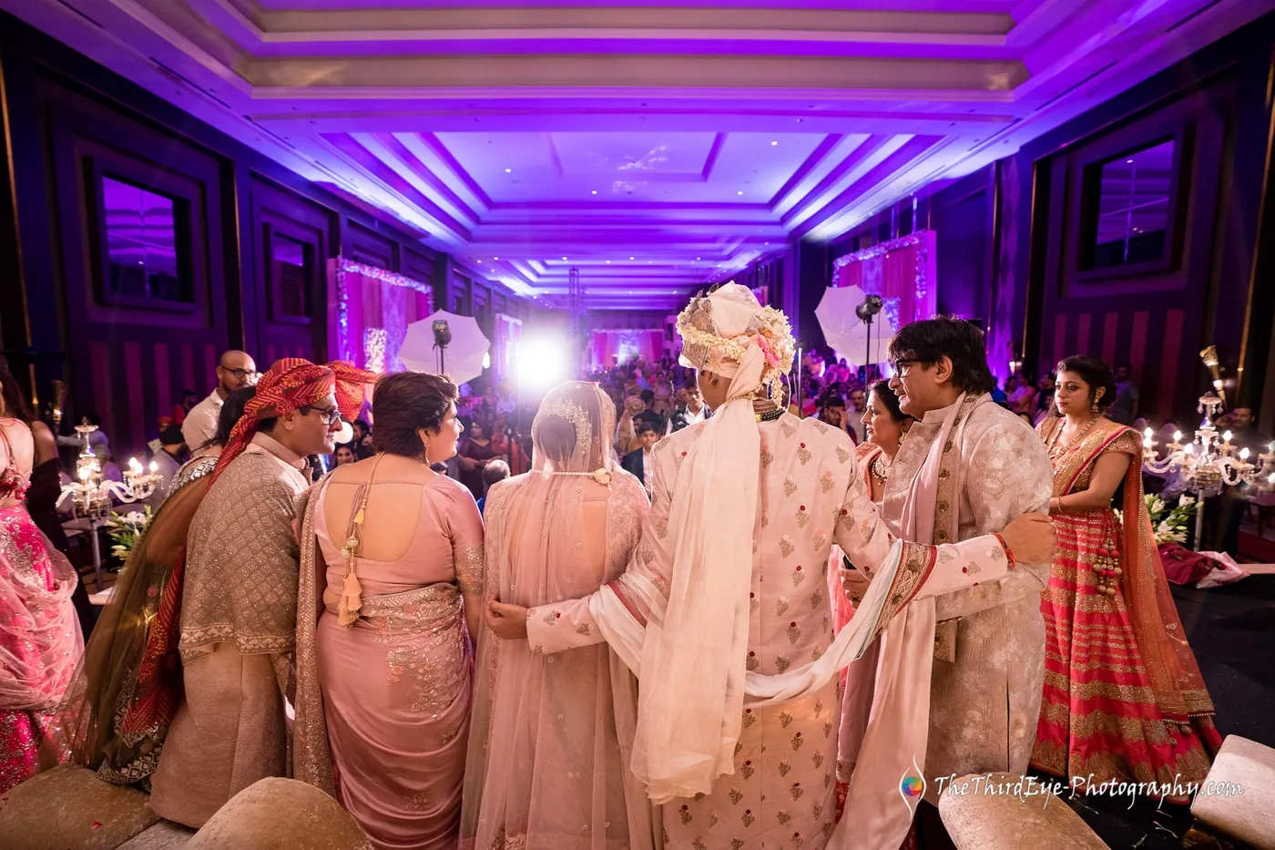 A hall bathed in purple light as family members cluster close around the couple