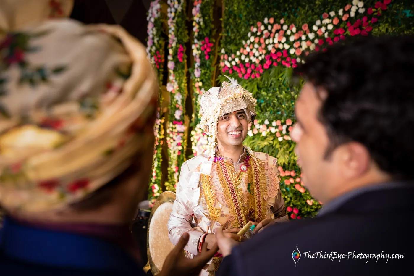 A man in a turban turns to speak with a man in a blue shirt, the groom behind them