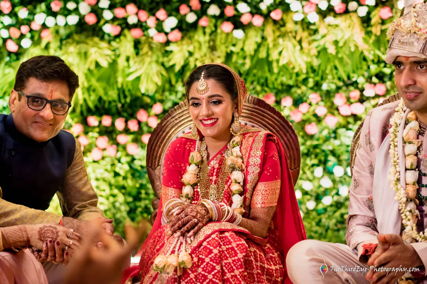 The bride beams as a man in a navy waistcoat leans in and the groom sits beside her