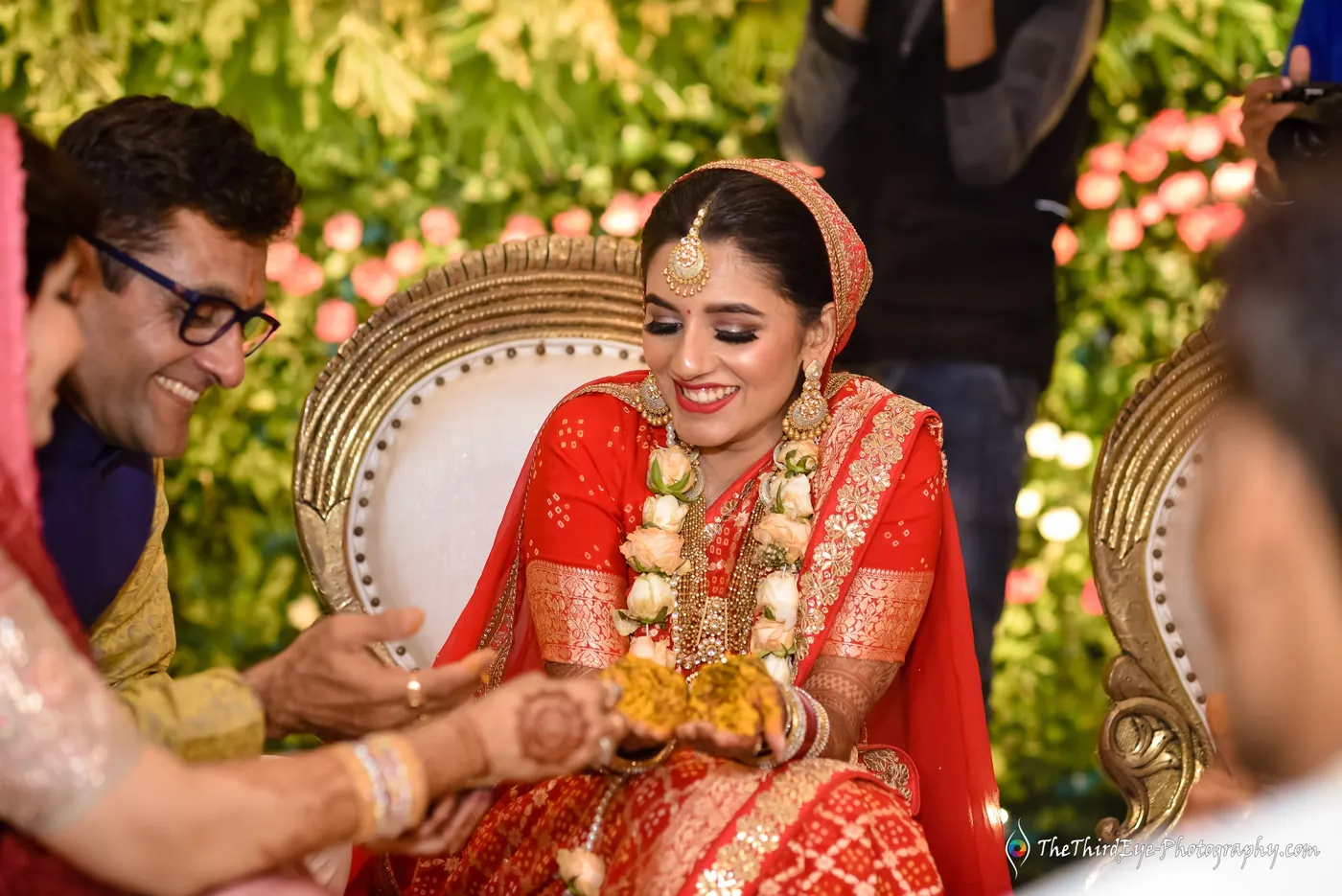 The bride laughs as a man in glasses presses turmeric into her hands