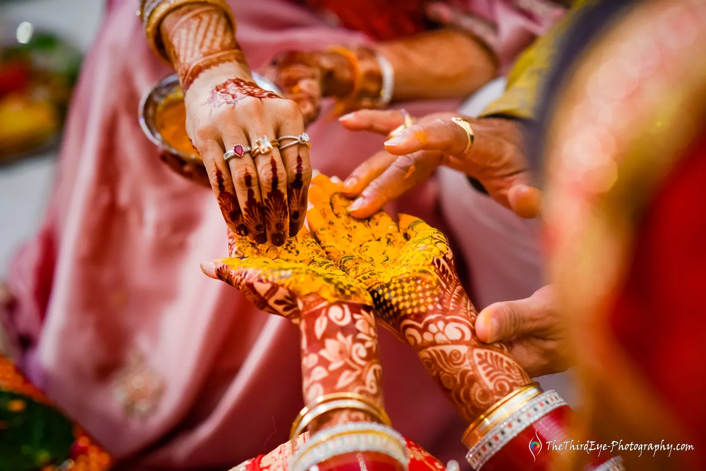 Close view of henna decorated hands pressing yellow turmeric paste into another pair of hands