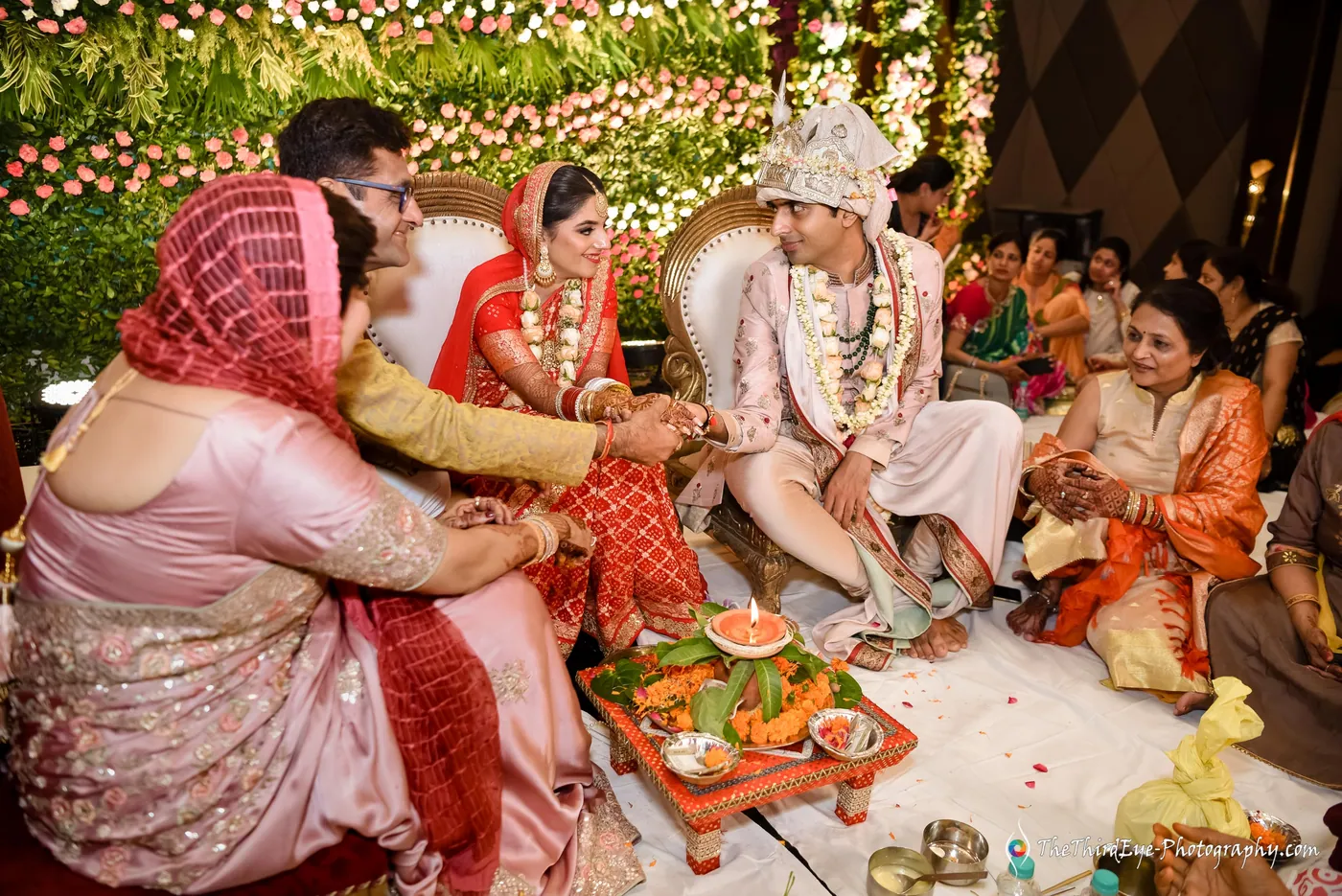 The family sit close around a ritual platform as the groom and bride take part, women watching