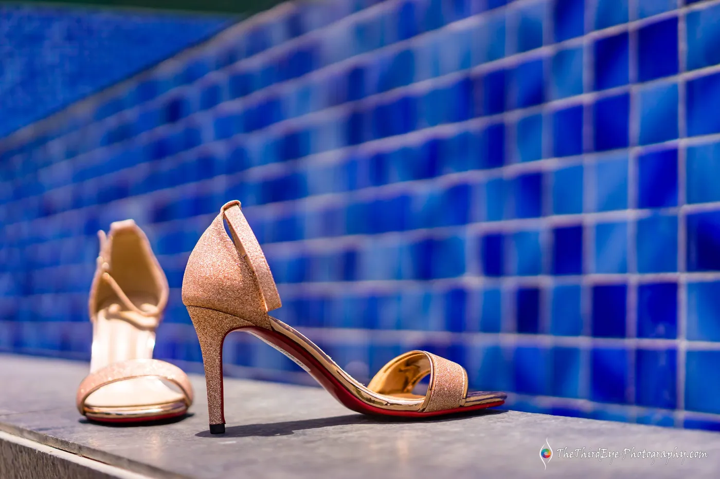 Gold high heels rest on a ledge against a wall of deep blue tiles