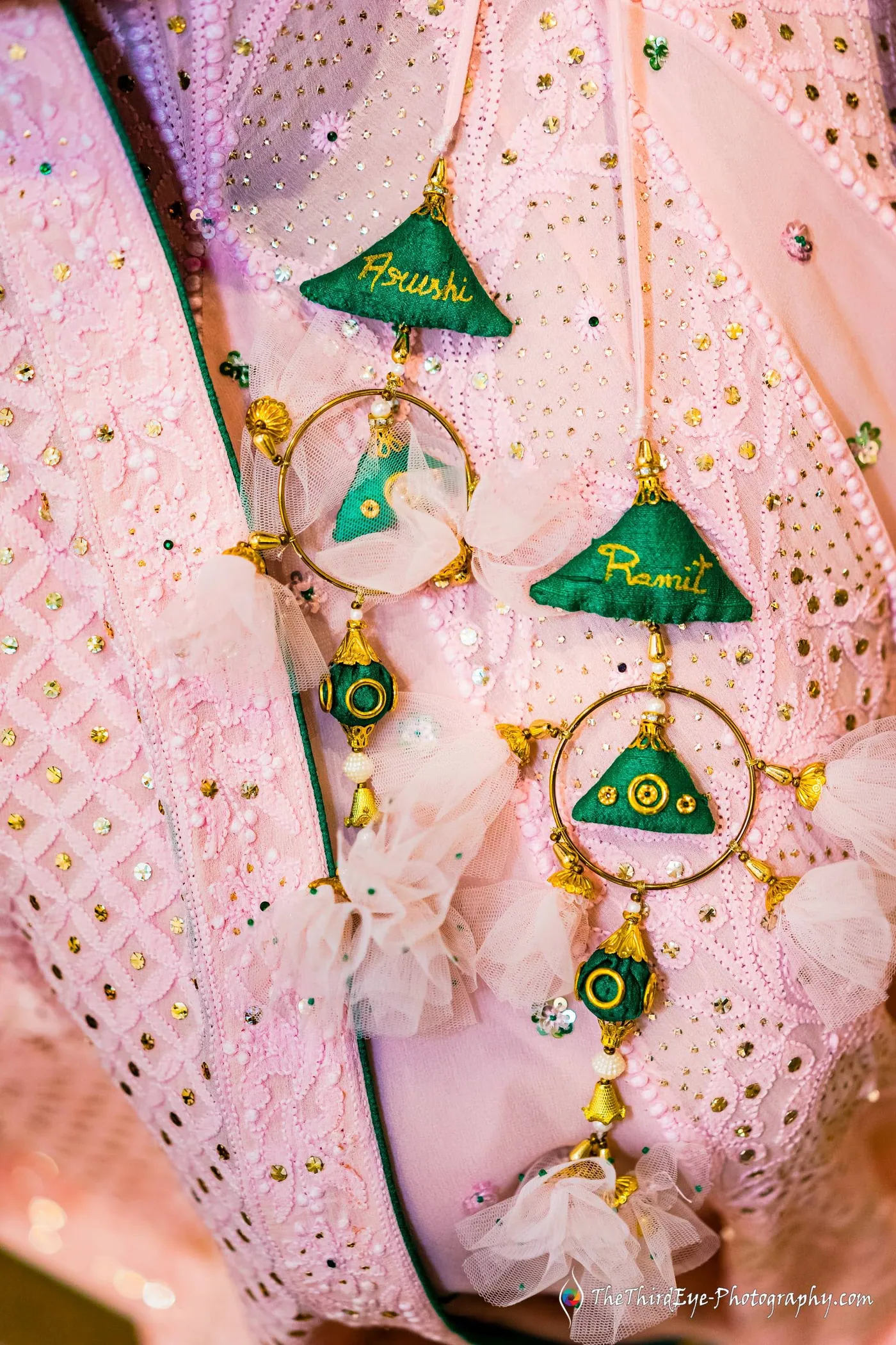 Close view of a pink lehenga with green triangle motifs and gold tassels, mirror work catching the light