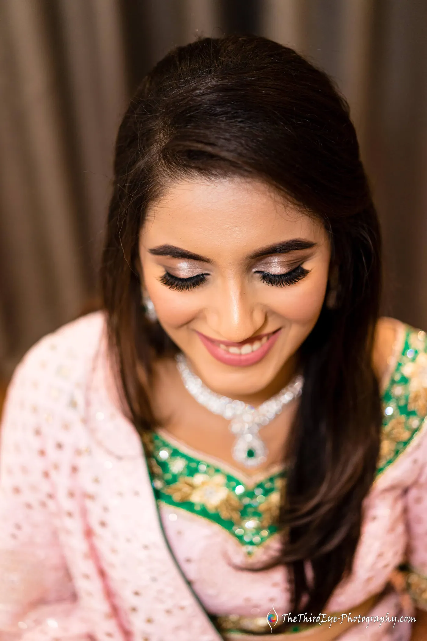 A woman with long dark hair smiles down in a pink outfit trimmed in green