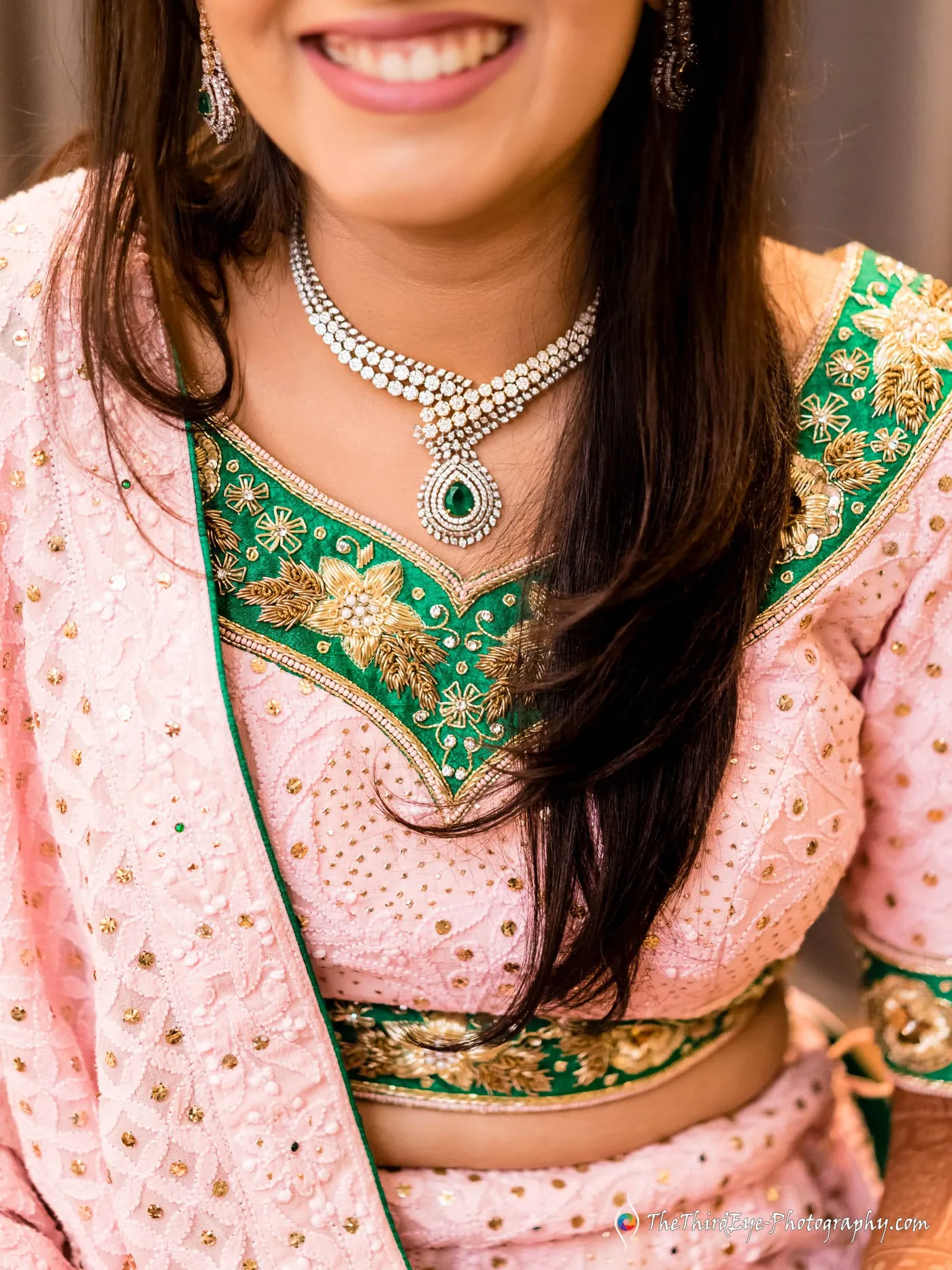A woman in a pink and green embroidered outfit smiles softly, her long hair falling over one shoulder