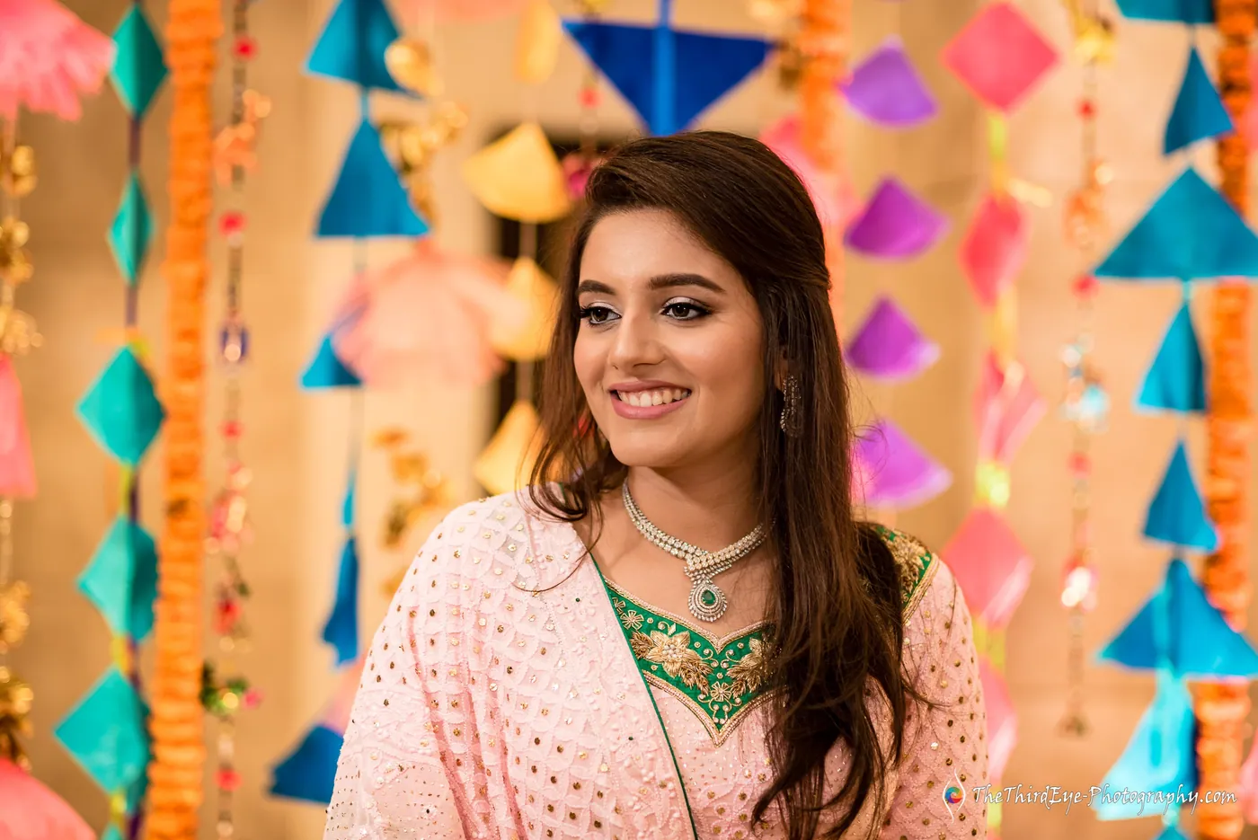 The bride smiles softly in front of hanging paper kites in pink, orange and blue