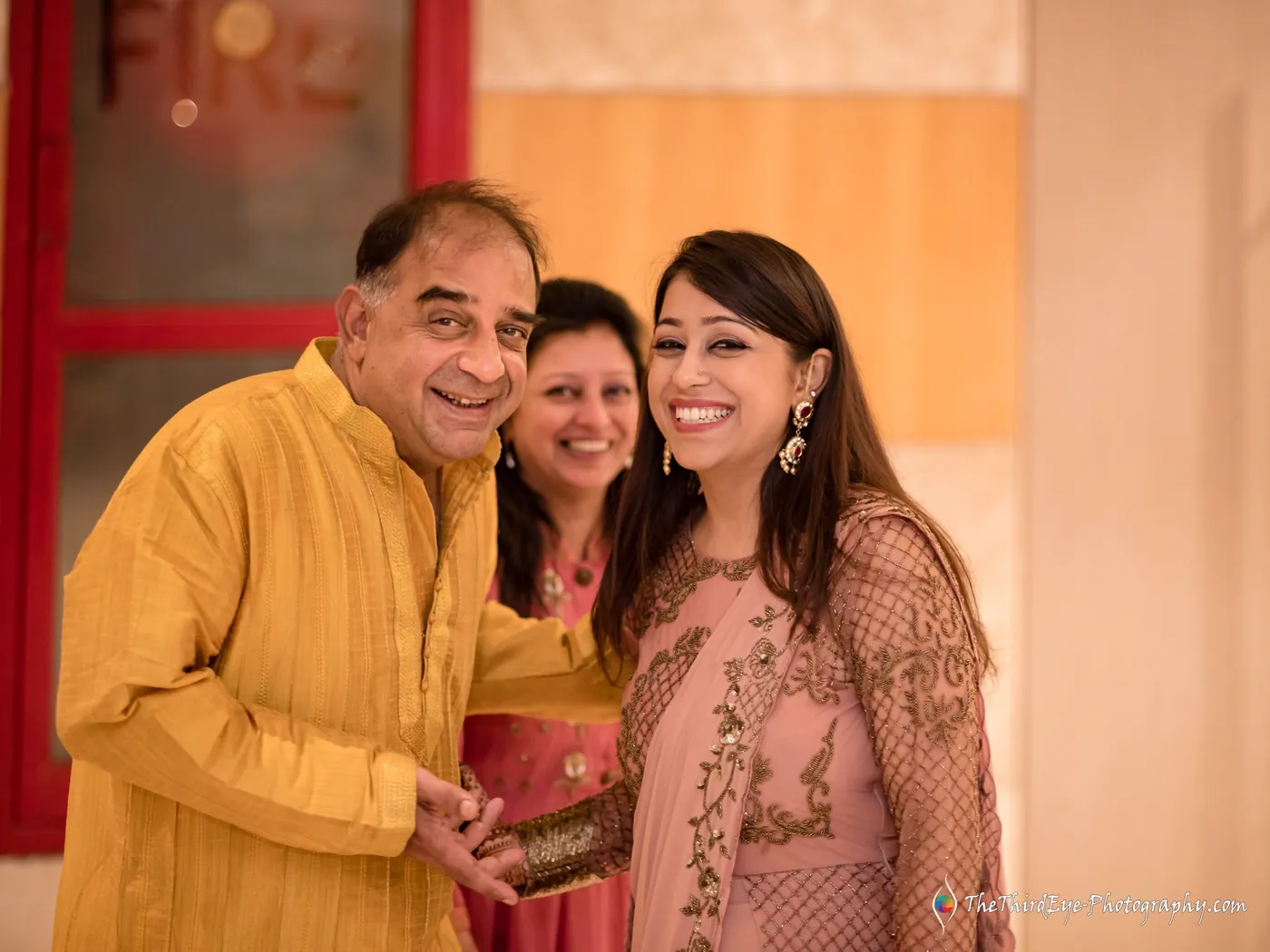 A man in yellow and a woman in pink stand cheek to cheek as another woman peeks in behind