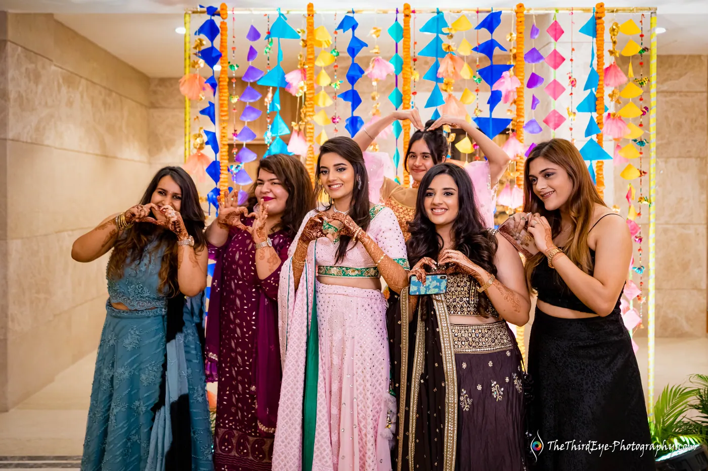 Seven women make heart shapes with their hands in front of hanging paper kites