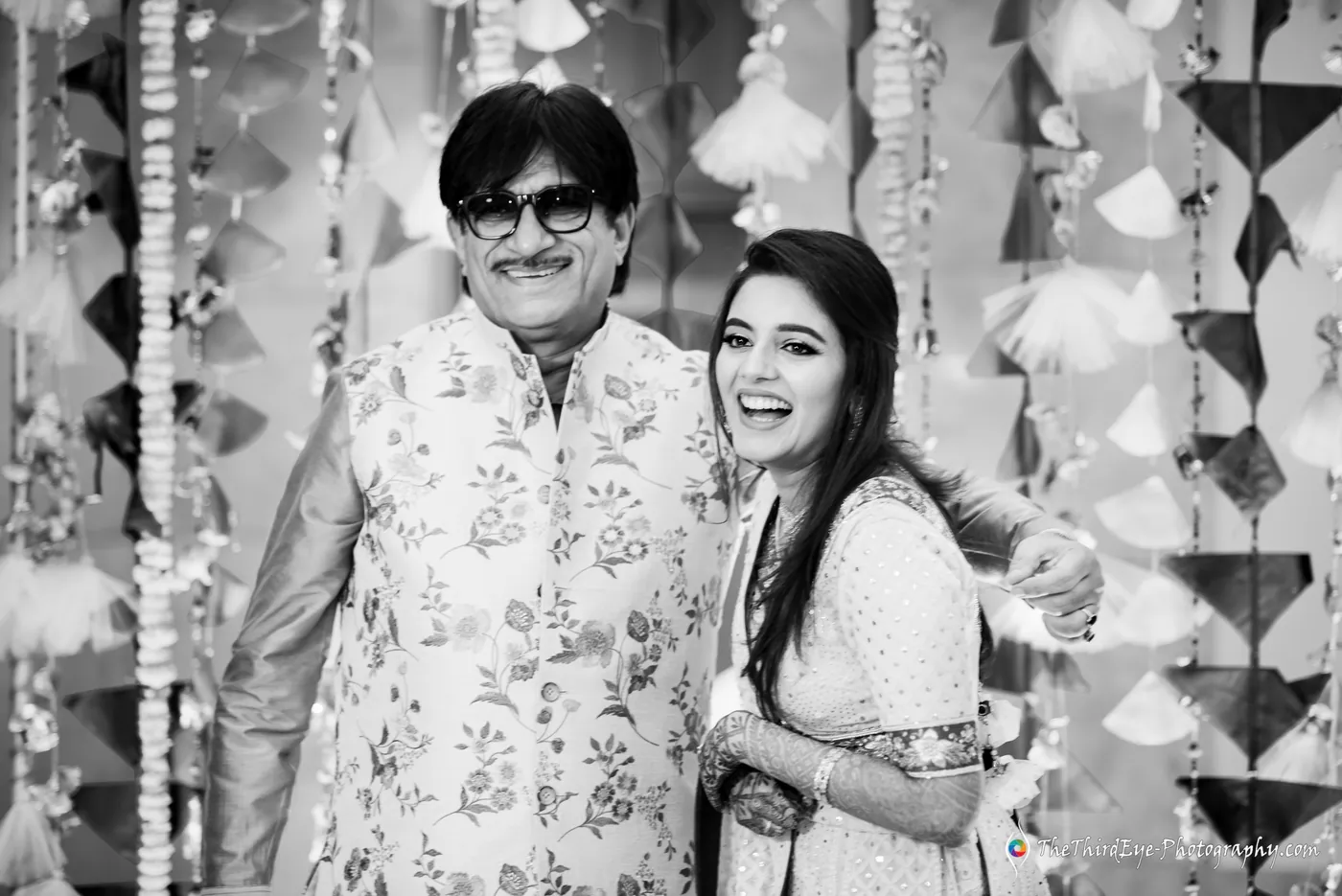 Black and white man in glasses and a floral jacket beams beside the bride, who laughs with him