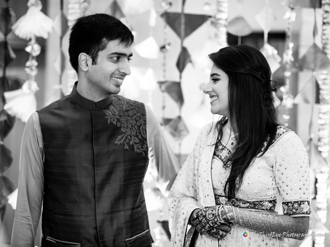 Black and white frame of Ramit and Arushi looking at each other and smiling, he in a textured waistcoat