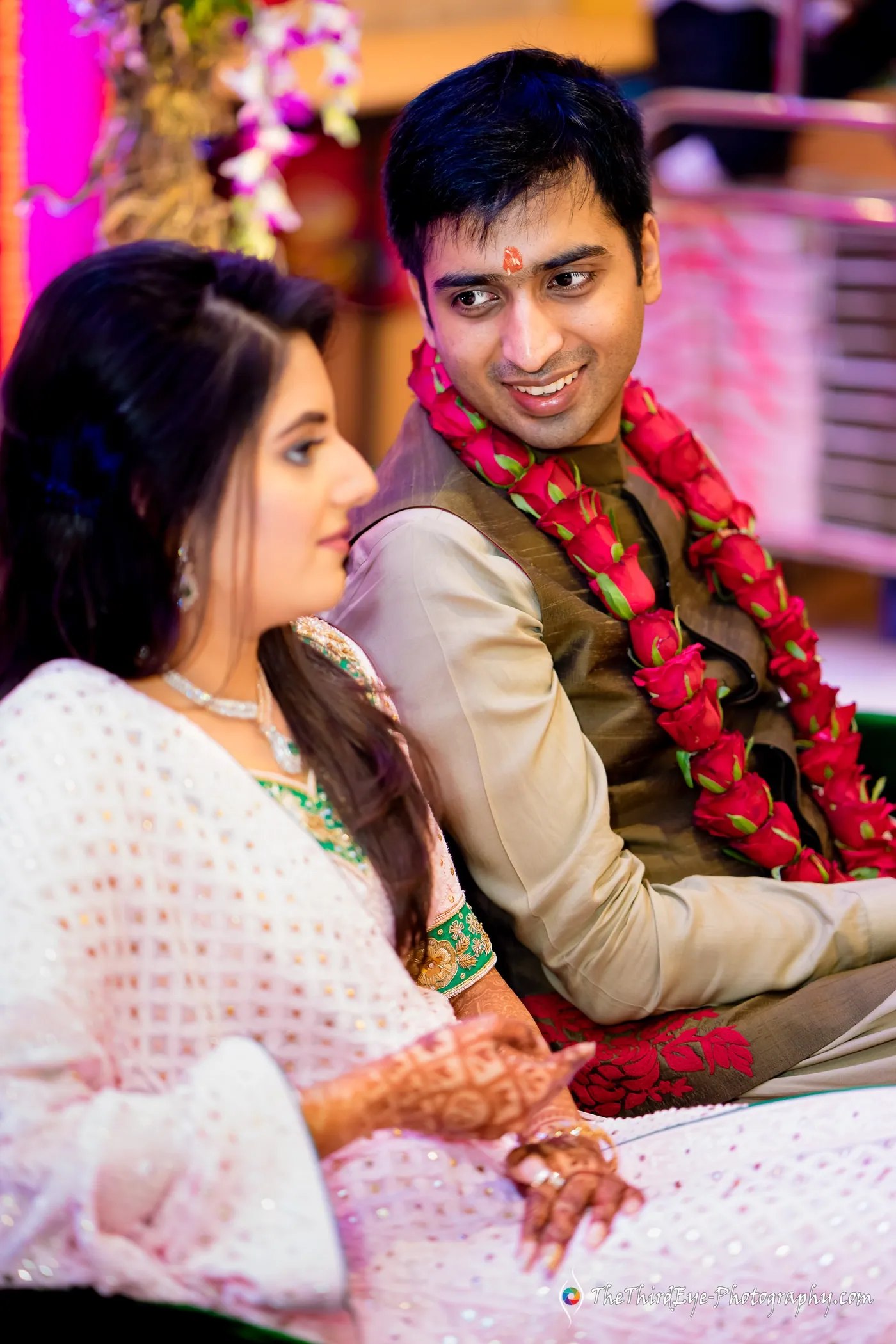 Ramit in a red flower garland sits close to Arushi, both smiling in a warm moment together