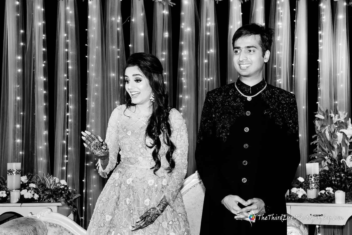 Black and white frame of Arushi laughing on stage as Ramit looks on in a dark embroidered jacket