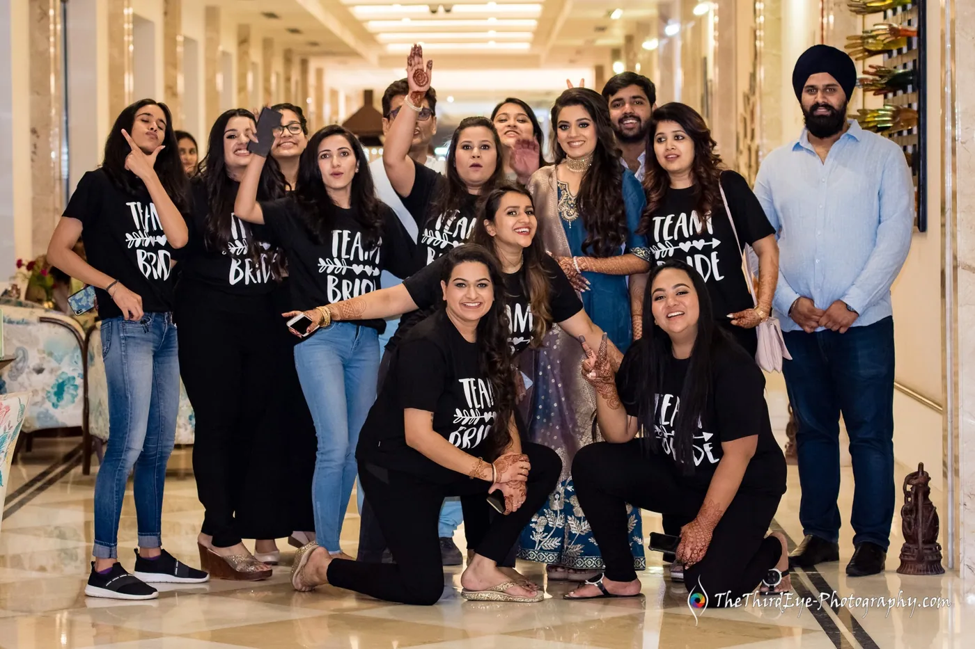 A group in black team t-shirts crowd into a hotel corridor, some kneeling, posing and laughing for the camera