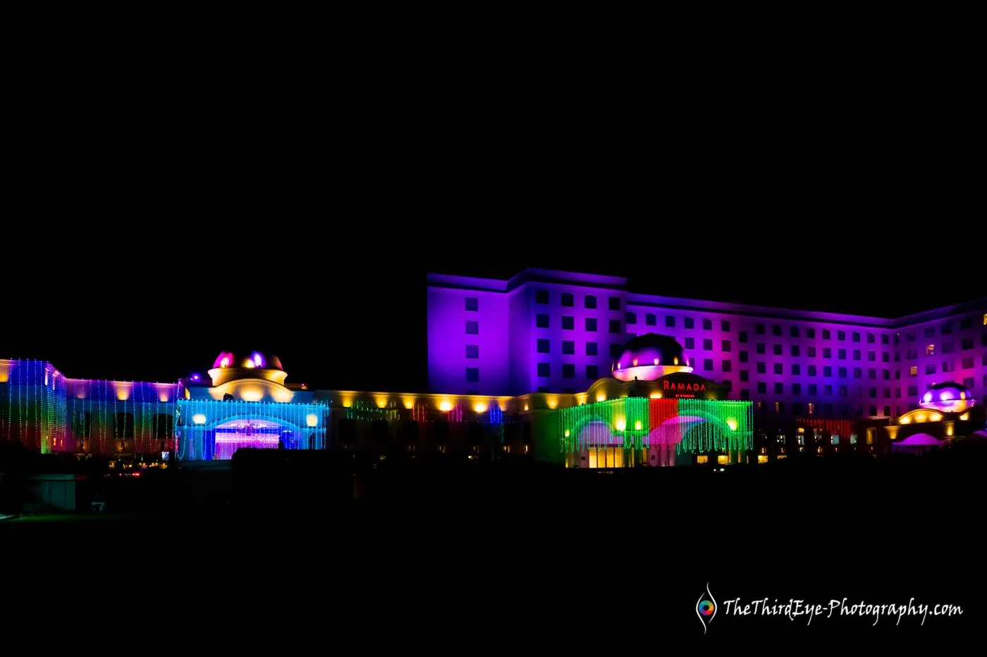 The Ramada hotel at night, its roofline outlined in pink, green and blue lights