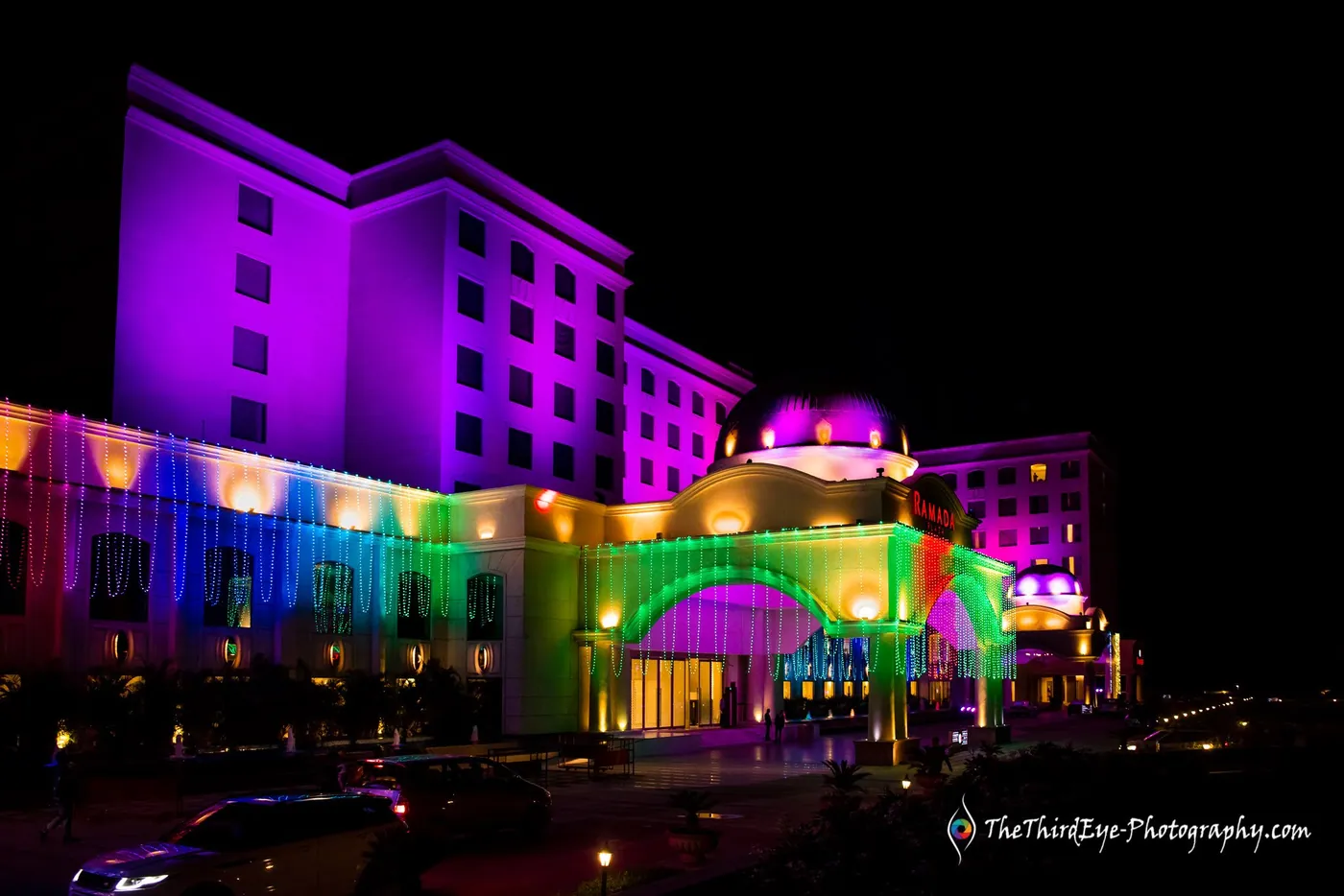 Hotel facade lit in purple, pink and green against the black sky, all the way to its dome