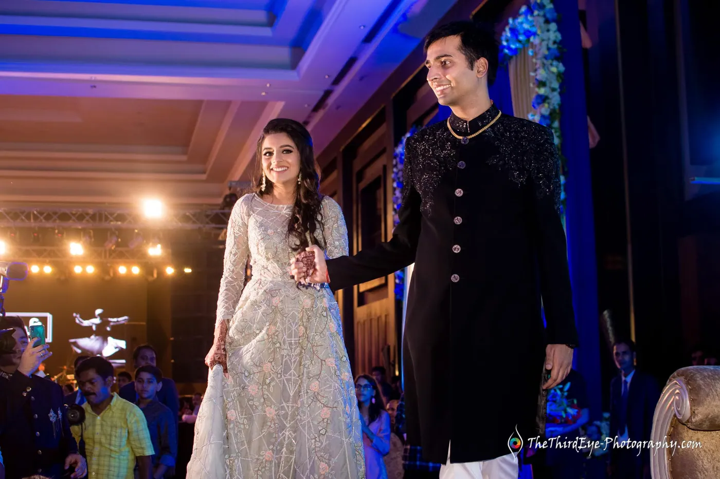 Ramit and Arushi step out together onto the stage, she lifting her ivory gown, he in a dark sherwani