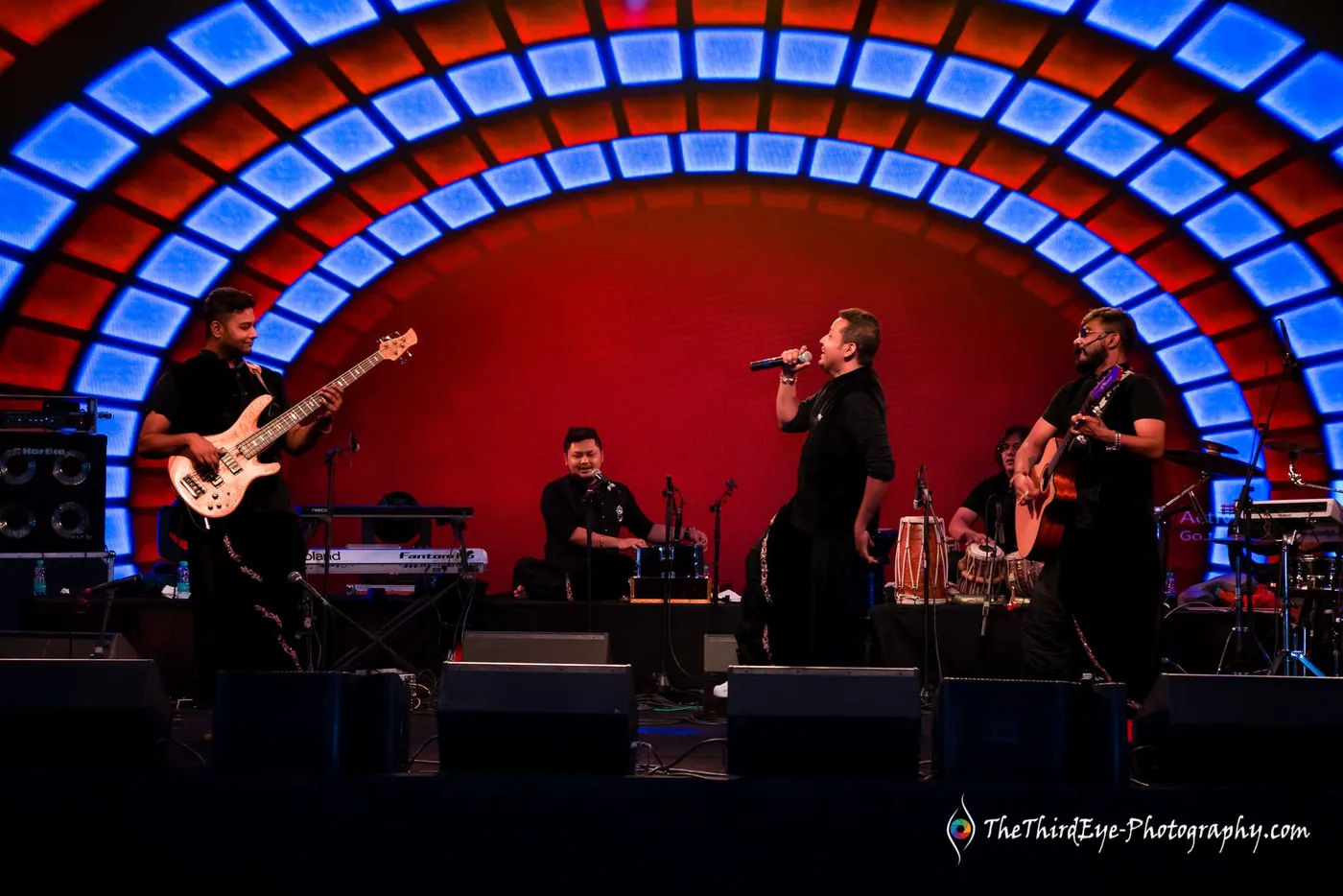 A band plays on a red stage framed by an arch of glowing blue panels