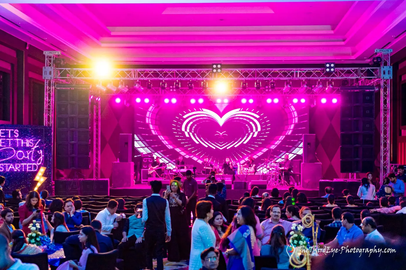 A pink heart shaped screen glows above the stage as guests fill the ballroom seats