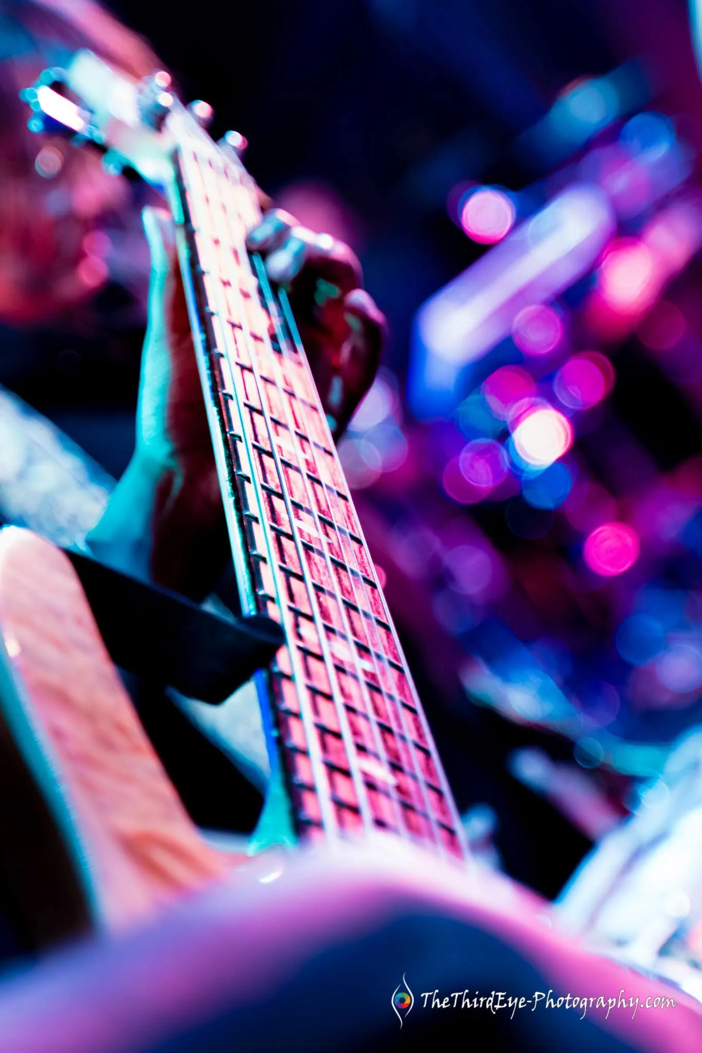 Close view of guitar strings and frets in blurred pink and purple light