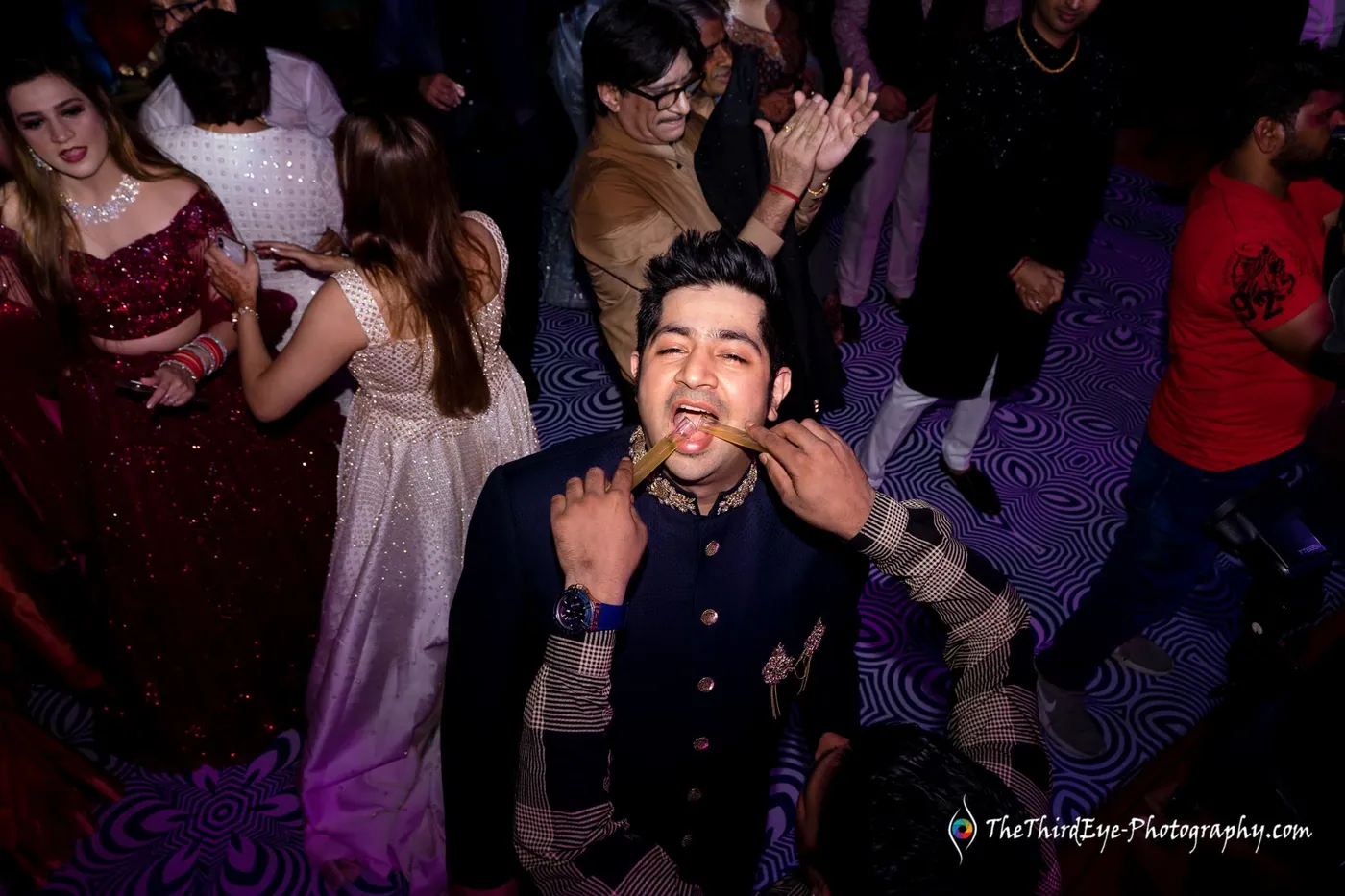 A man in a navy jacket shouts with joy on a crowded dance floor while women dance behind him