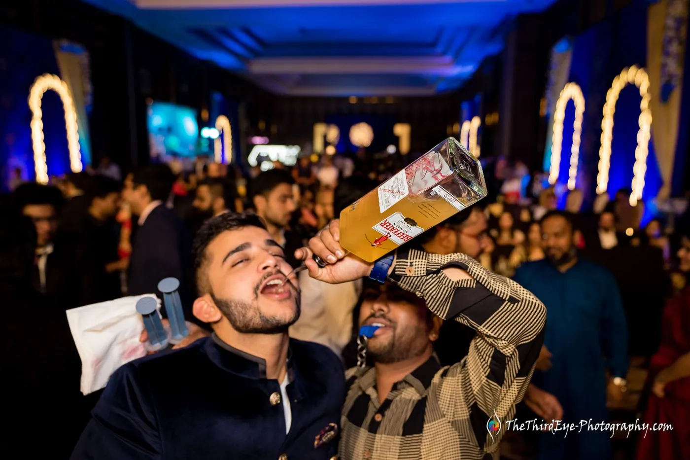 A man tips a large bottle to his lips while friends cheer around him in the packed hall