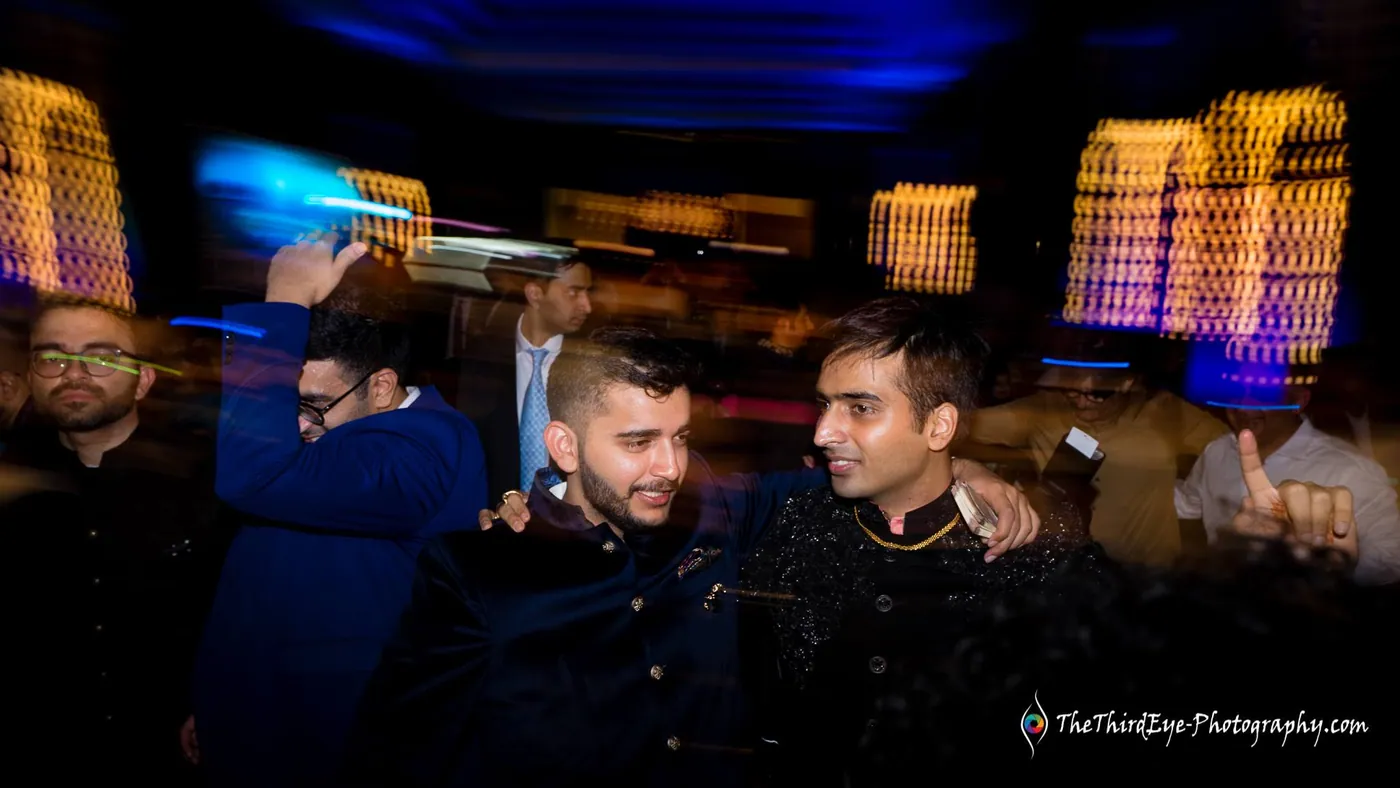 Slow shutter blur of men in dark jackets dancing together under warm hanging lights