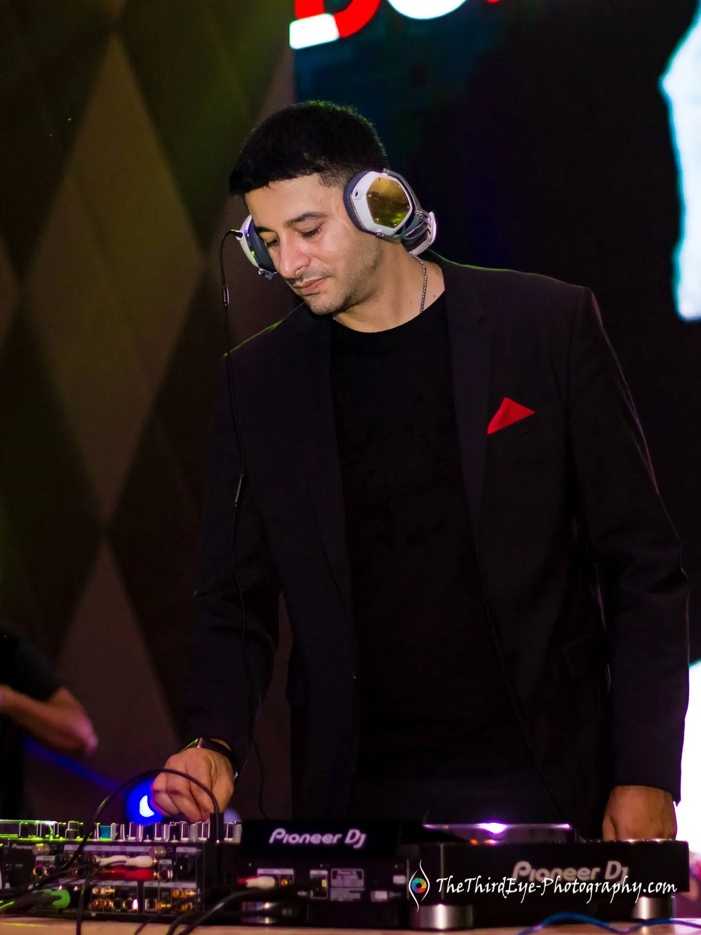 The DJ, Zulfi Syed, wears headphones and looks down at the decks in a dark jacket